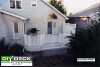A low single level medium size deck with a privacy screen and step lights attached to a large white house.