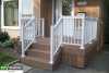Small composite porch with a white aluminum railing attached to the front of a red brick house.